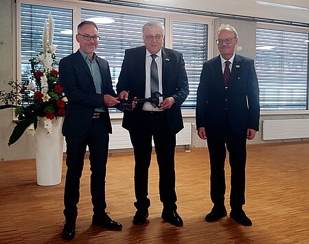 Drei Personen, einer davon übergibt einen großen Schlüssel