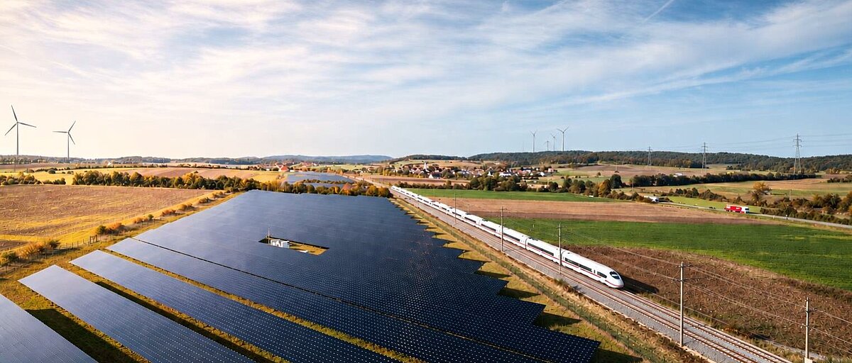Gleise mit ICE, Bundesstraße mit Lastwagen neben einem großen Photovoltaik-Feld