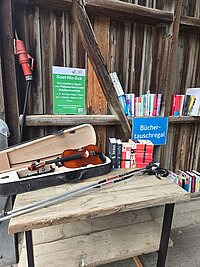 Verkaufstisch mit vielen verschiedenen Freizeitartikeln, einer Geige und Büchern im Hintergrund