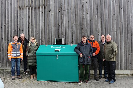 Gruppe von Personen steht rund um den Konfiskatbehälter