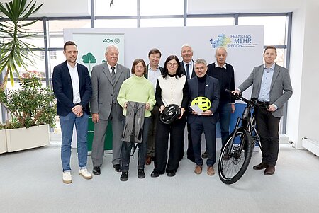 Neun Personen stehen mit Fahrradausstattung und einem E-Bike vor der Fotowand