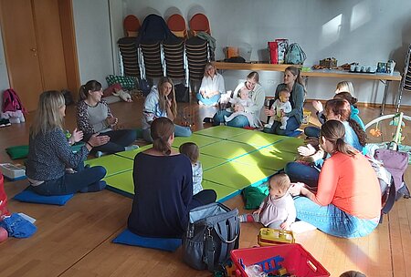 Gruppe von Erwachsenen und Babys sitzt auf dem Boden und spielt