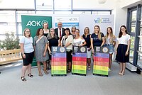 Viele Personen stehen vor einer Fotowand und halten UV-Index-Tafeln